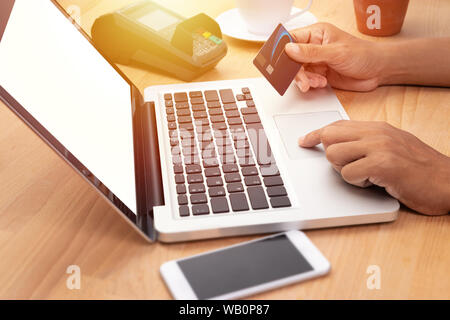 Homme tenant une carte de crédit et d'achat en ligne de faire le paiement via ordinateur portable ordinateur portable avec écran blanc au lieu de travail Banque D'Images