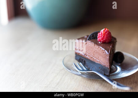 Un morceau de gâteau au chocolat avocat cru avec un brillant framboise et un cookie oreo sur le dessus. Banque D'Images