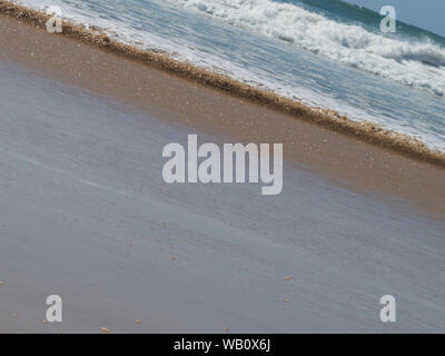 paysage de mer, lignes et couches de plage et de mer, avec le soleil attrapant le sable humide où ils se rencontrent et étincelant, pris sur un angle Banque D'Images