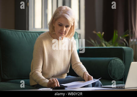 Projets de loi sérieux mature woman doing paperwork using calculator Banque D'Images