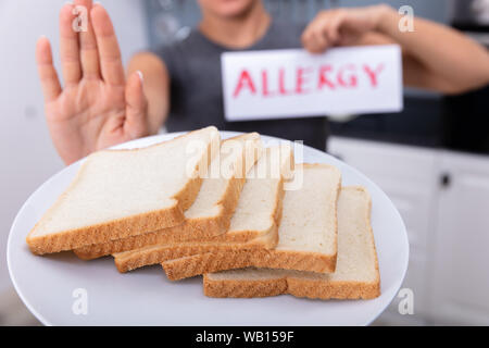 Jeune femme refusant tranche de pain sur la plaque à la carte texte Allergie Holding Banque D'Images
