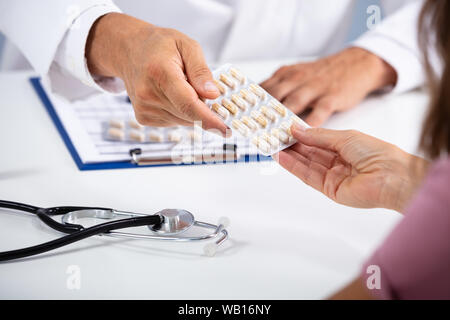 Les hommes de main du médecin donnant comprimés en plaquettes alvéolées de Female Patient In Clinic Banque D'Images