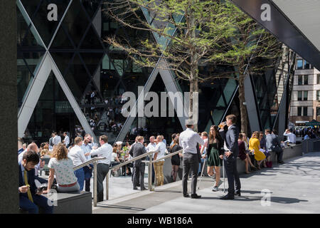 Les travailleurs de la ville de midi prendre un verre au soleil d'été sous le Swiss Re building (aka le Gherkin), dans la ville de Londres, le quartier financier de la capitale (aka le Square Mile), le 22 août 2019, à Londres, en Angleterre. Banque D'Images