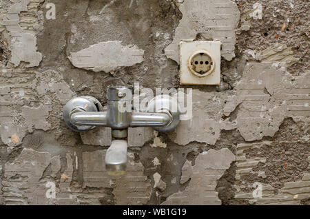 Ancien robinet de cuisine et d'un socket sur un mur gratté pendant les travaux de reconstruction Banque D'Images