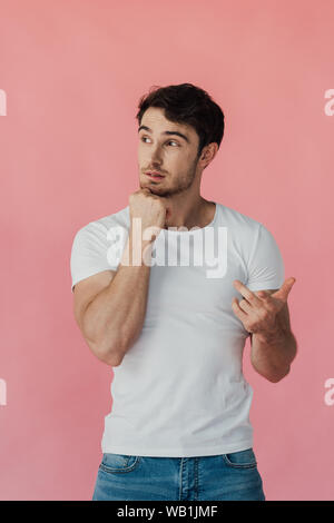 Homme musclé pensif en blanc T-shirt pour soutenir face avec fist et compte sur les doigts isolé sur pink Banque D'Images