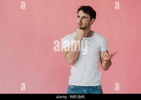 Homme musclé pensif en blanc T-shirt pour soutenir face avec fist et compte sur les doigts isolé sur pink Banque D'Images