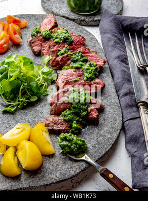 Tranches de steak de boeuf avec sauce au chimmichuri sur plaque de pierre grise Banque D'Images