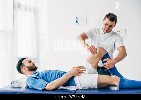 Physiothérapeute masser la jambe du joueur de football allongé sur la table de massage à l'hôpital Banque D'Images