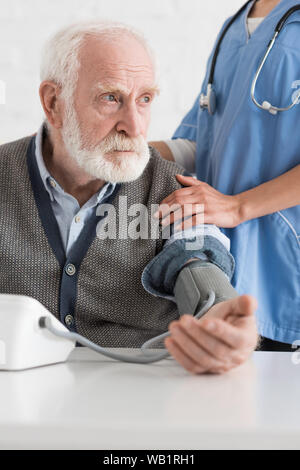 Portrait de l'infirmière mettant les mains sur l'homme aux cheveux gris, la mesure de la pression artérielle Banque D'Images