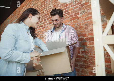 Construire l'avenir. Jeune couple a emménagé dans une nouvelle maison ou appartement. L'air heureux et confiant. La famille, déménagement, de relations, de premier accueil concept. Déballer leurs boîtes avec des livres et des plantes, placez-le sur les étagères. Banque D'Images