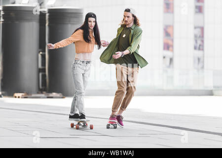 Couple heureux dans les vêtements de se tenir la main, à cheval sur la planche à roulettes dans la ville Banque D'Images