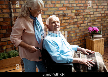 Cheerful senior femme debout près de personnes handicapées en fauteuil roulant, mari Banque D'Images