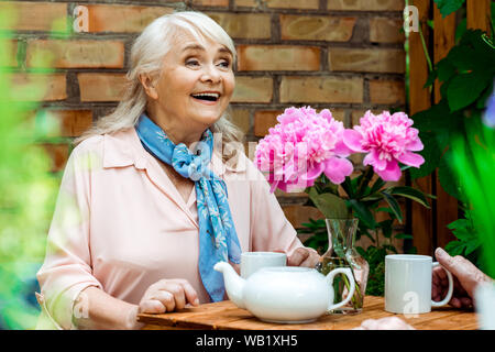 Focus sélectif de happy retired woman smiling près de fleurs roses Banque D'Images