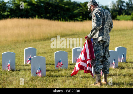 L'homme en uniforme militaire et cap holding american flag dans cimetière Banque D'Images