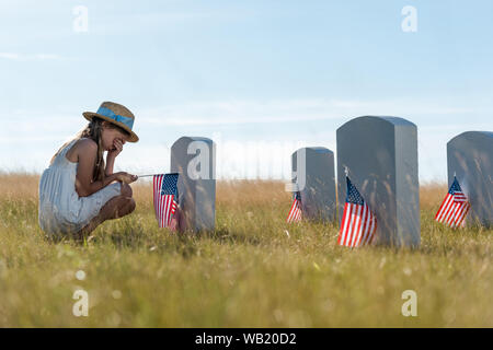 Focus sélectif de visage tout en couvrant l'enfant assis près de pierres tombales avec american flags Banque D'Images