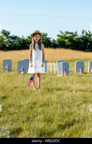 Focus sélectif de l'enfant en robe blanche debout sur cimetière avec drapeau américain Banque D'Images