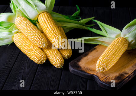 Maïs bonduel jaune juteux frais avec des feuilles vertes se trouve sur la table en bois Banque D'Images