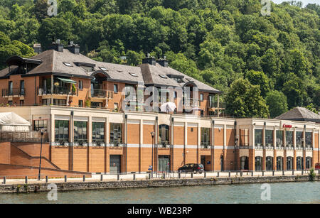 Dinant, Belgique - 26 juin 2019 : Beige et Rouge bâtisse en pierre du Casino et l'hôtel le long de la rivière Meuse soutenu par le feuillage vert. Banque D'Images