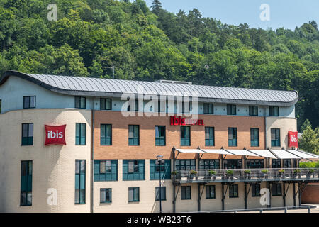 Dinant, Belgique - 26 juin 2019 : Beige et Rouge immeuble pierre de l'hôtel Ibis le long de Meuse soutenu par le feuillage vert. Banque D'Images