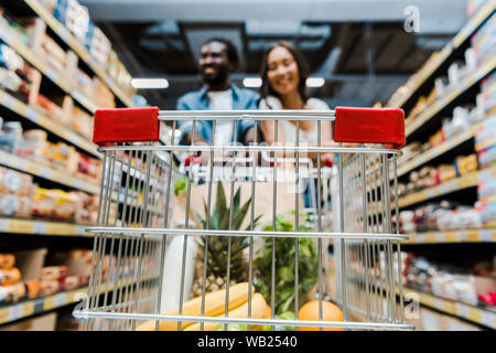 Focus sélectif des fruits dans votre panier près de l'heureux couple interracial en magasin Banque D'Images