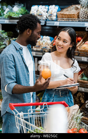 Portrait of happy asian girl près de african american man avec orange Banque D'Images