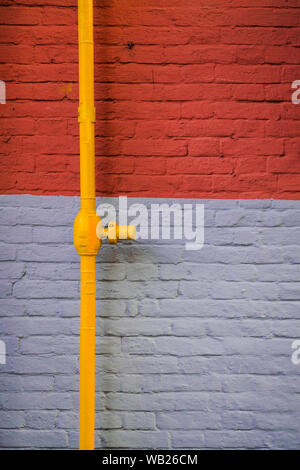 Gris et orange, mur de briques avec tube jaune Banque D'Images