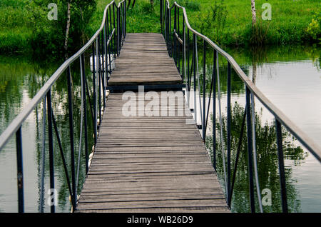 Un étroit pont en bois avec garde-corps en métal de l'autre côté de la rivière mène à la rive Banque D'Images