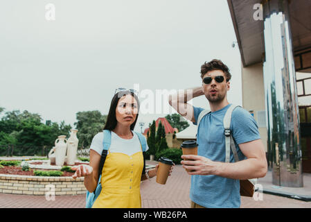 Homme choqué et asian woman holding tasses de papier avec du café Banque D'Images