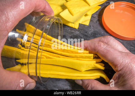 Près d'un coup de mains en plaçant un jaune vif, rawhide dentaire chien mâchonne dans un récipient de stockage en plastique. Banque D'Images