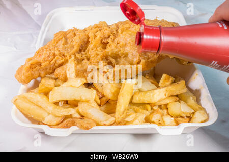 Près d'un repas à emporter frits battered fish and chips, avec du vinaigre est versé. Banque D'Images