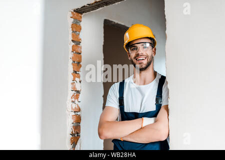 Heureux homme barbu à lunettes et casque smiling while standing with crossed arms Banque D'Images