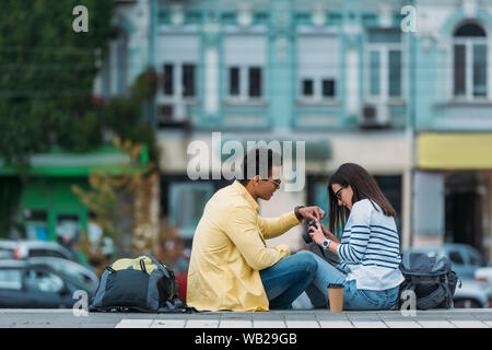 L'Interracial avec des sacs d'amis assis dans les escaliers et définition des propriétés de l'appareil photo Banque D'Images