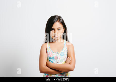 9-year old girl looking at camera. Elle est debout devant un mur blanc. Elle a l'air contrarié et déçu. Elle a de longs cheveux noirs. Elle a hispanic Banque D'Images