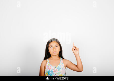 Une fillette de 9 ans est dirigé vers son côté droit. Elle est debout devant un mur blanc. Elle est souriante. Elle a de longs cheveux noirs. Elle a hispanic feat Banque D'Images
