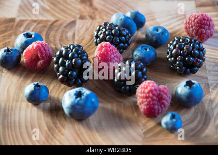 Les baies mûres lumineux du jardin sont dispersés sur une table en bois. Les bleuets, framboises, bleuets se trouvent sur la table dans l'été. Banque D'Images