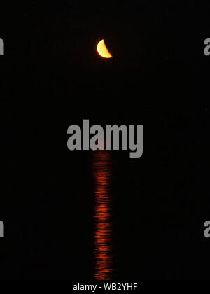 Sheerness, Kent, UK. 23 août, 2019. Météo France : un étrange à la demi-lune rouge se lève sur la mer dans Sheerness, Kent. Ce soir la lune est dans son dernier quart de la phase de lune (aussi connu comme le troisième trimestre), qui se produit à peu près 3 semaines après une Nouvelle Lune. 30 août verra une super lune noire (la survenue d'une deuxième nouvelle lune dans un mois). Credit : James Bell/Alamy Live News Banque D'Images