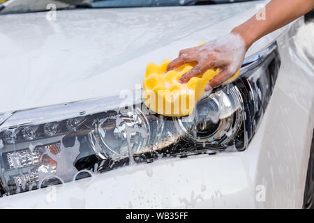 Main femme éponge jaune avec lave-phare feu de voiture moderne ou de nettoyage automobile. Concept de lavage de voiture Banque D'Images