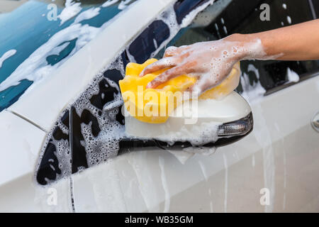 Femme la main avec une éponge jaune miroir côté lavage voiture moderne ou de nettoyage automobile. Concept de lavage de voiture Banque D'Images