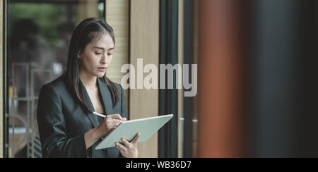 Portrait of attractive young businesswoman examinant les projets précédents sur tablette dans la salle de bureau moderne Banque D'Images