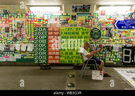 Man reading newspaper nonchalamment en face de la démocratie pro mur de Lennon à Hong Kong Banque D'Images