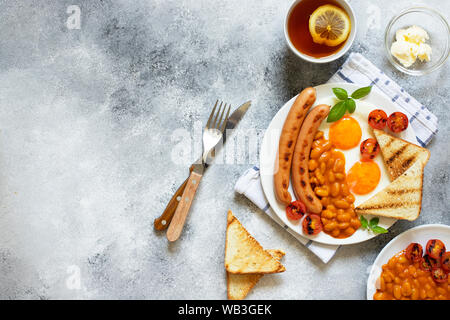 Petit déjeuner anglais avec saucisses frites, haricots, champignons, œufs frits, tomates cerises grillées. Fond gris Banque D'Images