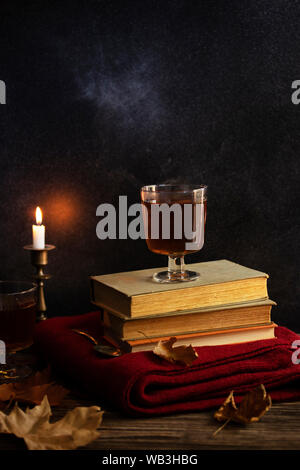 Une tasse de thé chaud, des livres, une couverture tricotée en laine, une bougie, feuilles d'automne sur une table en bois vintage. Ambiance cosy de l'automne. Clé faible. Copyspace. Banque D'Images