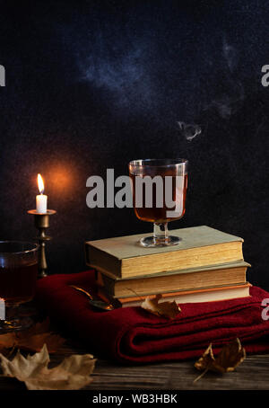 Une tasse de thé chaud, des livres, une couverture tricotée en laine, une bougie, feuilles d'automne sur une table en bois vintage. Ambiance cosy de l'automne. Clé faible. Copyspace. Banque D'Images