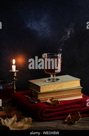 Une tasse de thé chaud, des livres, une couverture tricotée en laine, une bougie, feuilles d'automne sur une table en bois vintage. Ambiance cosy de l'automne. Clé faible. Copyspace. Banque D'Images