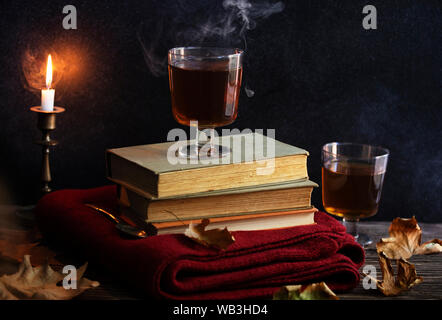 Une tasse de thé chaud, des livres, une couverture tricotée en laine, une bougie, feuilles d'automne sur une table en bois vintage. Ambiance cosy de l'automne. Clé faible. Copyspace. Banque D'Images