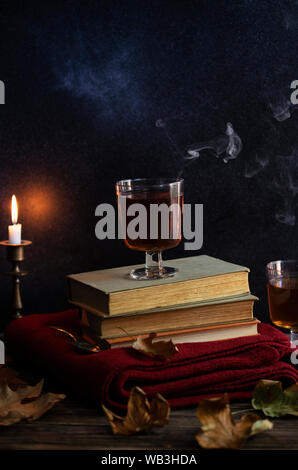 Une tasse de thé chaud, des livres, une couverture tricotée en laine, une bougie, feuilles d'automne sur une table en bois vintage. Ambiance cosy de l'automne. Clé faible. Copyspace. Banque D'Images