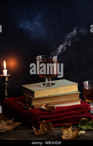 Une tasse de thé chaud, des livres, une couverture tricotée en laine, une bougie, feuilles d'automne sur une table en bois vintage. Ambiance cosy de l'automne. Clé faible. Copyspace. Banque D'Images