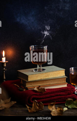 Une tasse de thé chaud, des livres, une couverture tricotée en laine, une bougie, feuilles d'automne sur une table en bois vintage. Ambiance cosy de l'automne. Clé faible. Copyspace. Banque D'Images