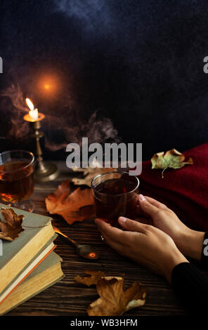 Jeune fille tenant une tasse de thé chaud dans ses mains. Humeur d'automne. Tasse de thé sur une table en bois d'époque, des bougies, les feuilles d'automne, books, plaid laine Banque D'Images