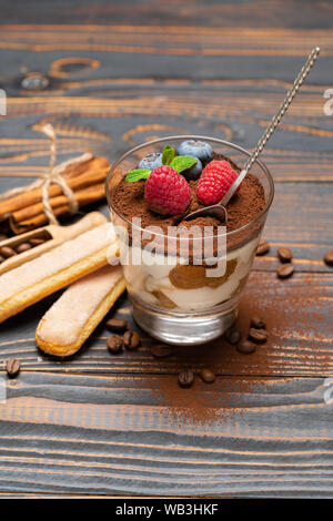 Dessert tiramisu classique avec les bleuets et les fraises dans une coupe en verre et les biscuits savoiardi sur fond de bois Banque D'Images